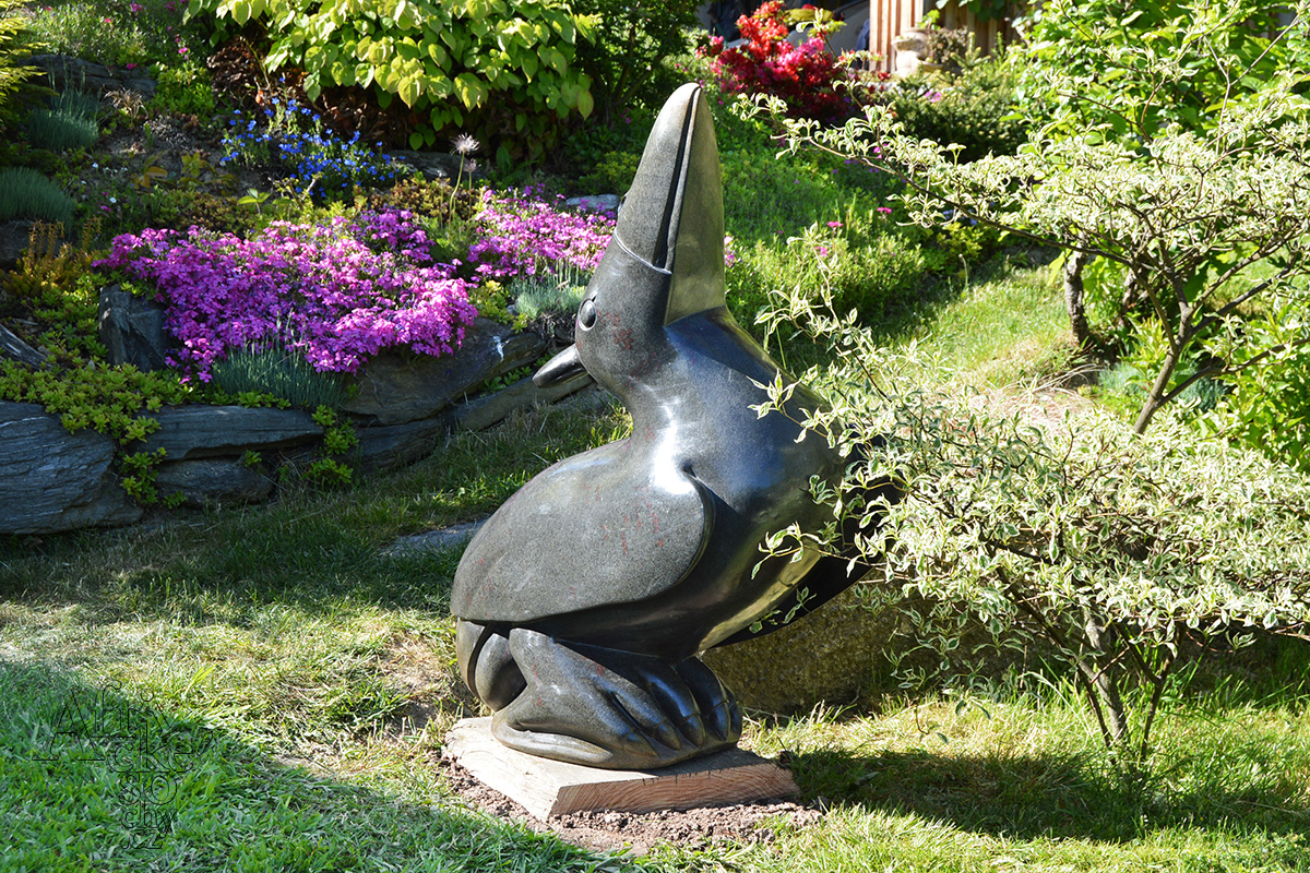 Kamenná socha ptáka v rozkvetlé zahradě od zimbabwského sochaře Uxoriuse Matemery